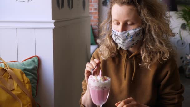 Frau mit Maske trinkt während der Coronavirus-Pandemie rosa Kaffeelatte im Café. — Stockvideo