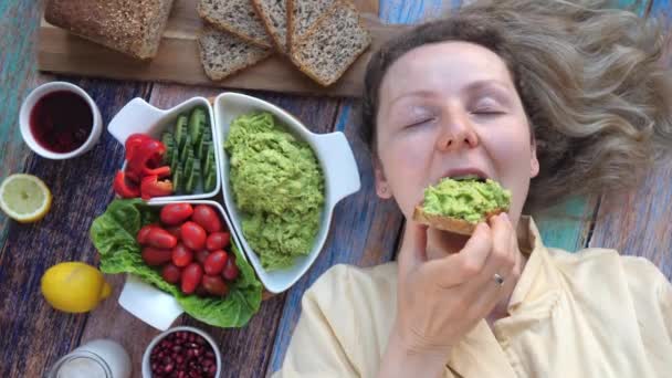 Joven mujer sonriente comiendo tostadas de aguacate en casa. — Vídeos de Stock