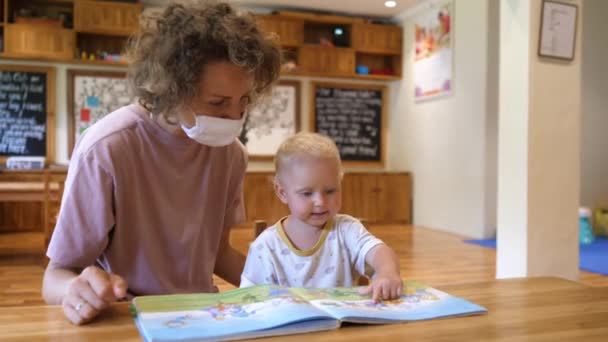 Joven madre soltera educa a su bebé con la lectura divertida. Actividades de aprendizaje de niños pequeños durante covid-19 — Vídeos de Stock