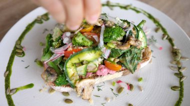 Üstünde farklı sebzeler olan vejetaryen tostun üzerine limon sıkma görüntüsü.