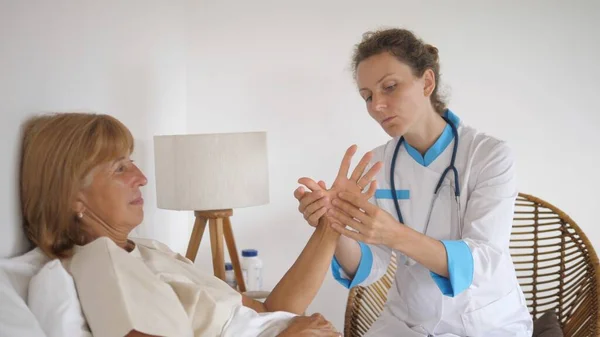 Private GP doctor examining joints and bones of patients hand, checking for arthritis during house call