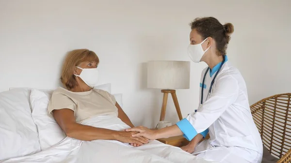 Private doctor visiting middle aged patient at home, treats and comforts her