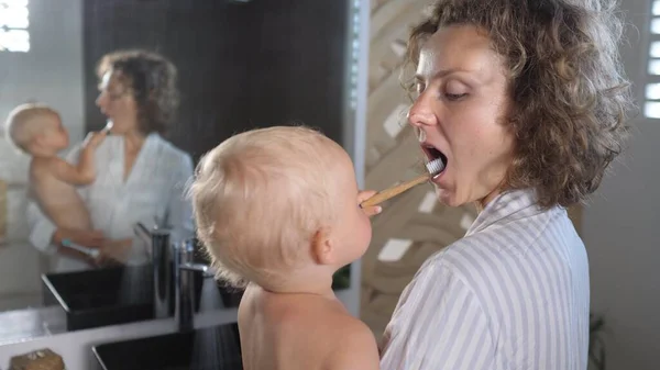 Joven caucásico madre sosteniendo su bebé cepillos dientes juntos — Foto de Stock