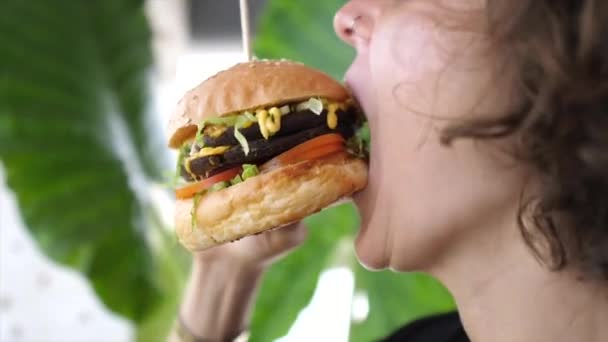 Primer plano de la joven mujer caucásica mordiendo hamburguesa vegana con gran apetito — Vídeo de stock