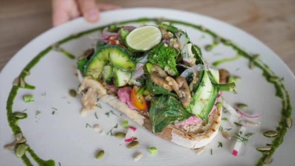 Auf dem Holztisch wird Teller von oben mit fantastischem veganem Sandwich serviert, belegt mit Tonnen von Gemüse — Stockvideo