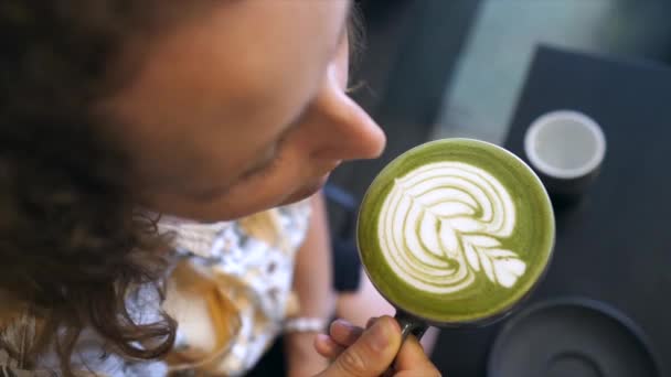 Widok z góry dziewczyny biorąc łyk matcha zielonej herbaty latte z latte sztuki na nim. Zdrowe opcje napojów na bazie roślin — Wideo stockowe