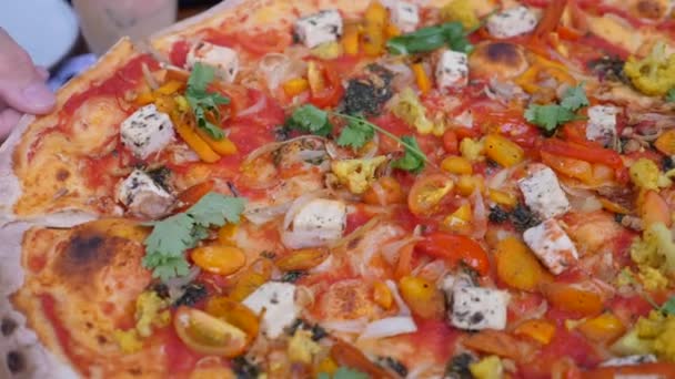 Mano tomando una rebanada de pizza vegana rematada con un montón de verduras y queso sin plantas y lácteos. Dieta vegetal — Vídeos de Stock