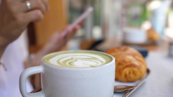 Ręka robi kubek z matcha zielonej herbaty latte. Smartfon rozmyty w tle — Wideo stockowe