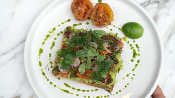 Zdravé chutné Veganské brunch. Pohled shora na ručně kladený talíř s avokádovým toastem na mramorovém stole. — Stock video