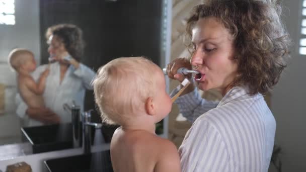 Jovem mãe branca segurando seu bebê escova os dentes juntos — Vídeo de Stock