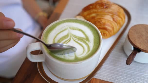 Ovanifrån av sked tar skum från matcha latte. Friska mejerifri dryck serveras med färsk croissant — Stockvideo