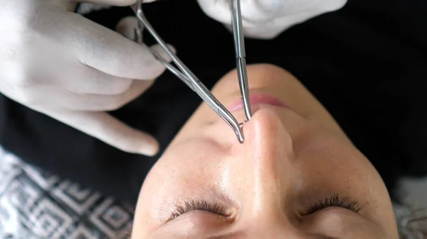 Body piercing process. Professional piercer in the disposable gloves sets nose ring properly