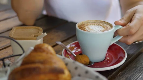Sluit van de hand het plukken van een kopje cappuccino te drinken. Koffie geserveerd met een gratis koekje aan de zijkant. — Stockfoto