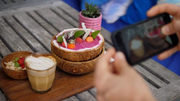 Smartphone met foto van tropische smoothie kom met koffie latte geserveerd op houten dienblad. Voedsel delen op sociale media — Stockfoto