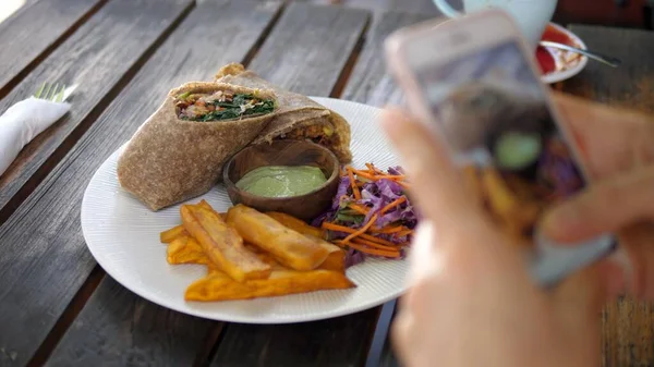 Handen nemen van foto 's van veganistische lunch bestond uit wrap, saus, koolsla en zoete aardappelen aan een kant. Concept voor voedselbloggen — Stockfoto