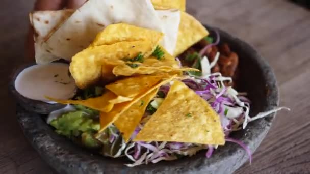 Close-up van handdraaiende stenen kom met veganistische snacks in Mexicaanse stijl: nacho 's, rode bonen, guacamole en saus. Veganistisch straatvoedsel — Stockvideo