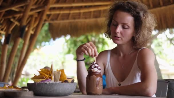 Chica caucásica almorzando sola en un restaurante de playa, mira detrás de su hombro. Concepto de viaje en solitario — Vídeos de Stock