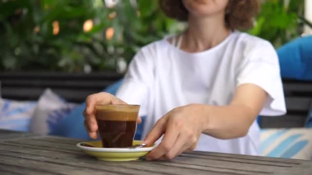 Chica rubia intenta su café negro servido en un vaso. Relajarse en la cafetería tropical — Vídeos de Stock