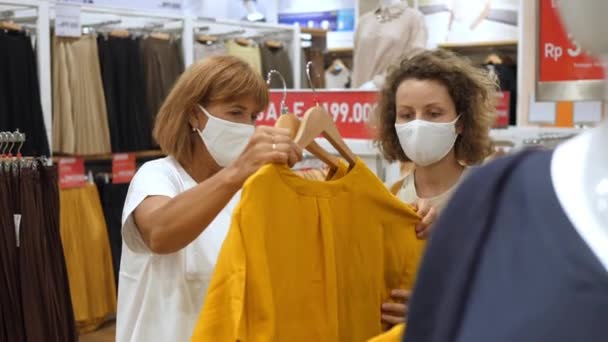 Moeder en dochter in beschermende gezichtsmaskers kiezen shirt in kledingwinkel. — Stockvideo