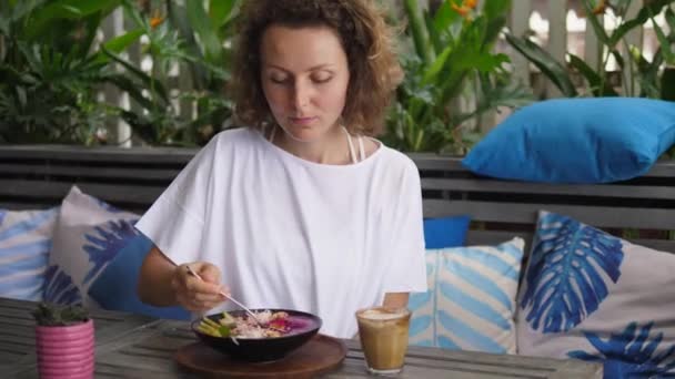 Caucásico chica comiendo su tropical smoothie bowl con gran placer en un restaurante al aire libre — Vídeos de Stock