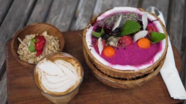 Tropikal kahvaltı manzarası hindistan cevizi kabuğunda servis edilen smoothie ve yanında müsli ile birlikte bardakta kahve içmekten ibaretti. Hepsi ahşap tepside