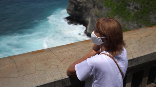 Vacanze durante la pandemia di Covid-19. Lady in una maschera protettiva bianca apprezzare la splendida vista dell'oceano dal ponte di osservazione — Video Stock