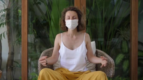 Vit kvinna med en skyddande ansiktsmask som utövar yoga i ett utrymme fullt av växter. Begreppet psykisk hälsa — Stockvideo