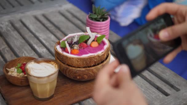Widok z góry wegańskie śniadanie smoothie miski kokosowe serwowane na drewnianej desce z mlecznych wolne latte jest fotografowany za pomocą smartfona — Wideo stockowe