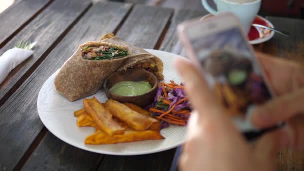 Hands taking picture of vegan lunch consisted of wrap, sauce, coleslaw and sweet potatoes on a side. Food blogging concept — Stock Video