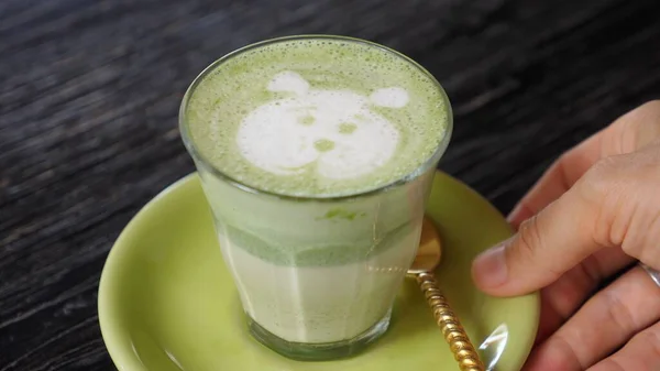 Mano quitando un vaso de té matcha latte con arte de espuma facial de oso en ella — Foto de Stock