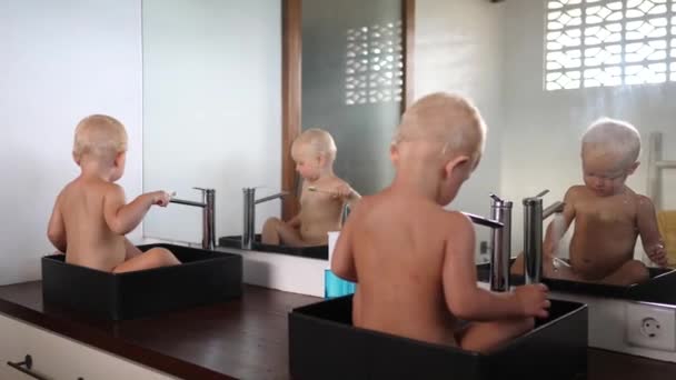 Dos niños gemelos caucásicos sentados en lavabos jugando con agua y cepillándose los dientes — Vídeo de stock
