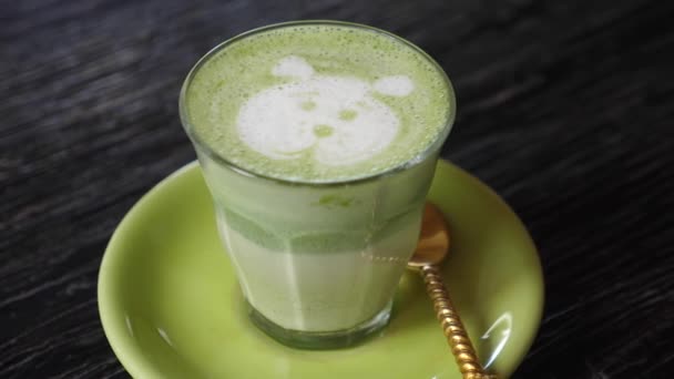 Ręka zabiera szklankę herbaty matcha latte z pianką na twarzy niedźwiedzia — Wideo stockowe