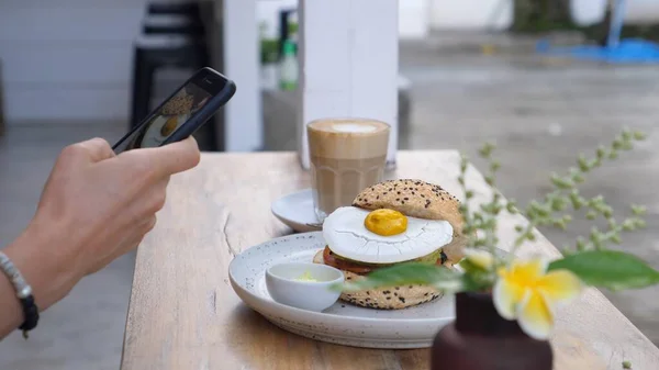 Hand nemen van foto 's van gezonde heerlijke wreedheid gratis veganistische lunch van een hamburger en cappuccino met een smartphone. — Stockfoto