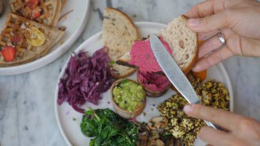 Bıçağın pancar ezmesini tostun üstüne sürüşünün en üst görüntüsü. Sağlıklı vejetaryen yemekleri ve diğer aperatifler bir tabakta 