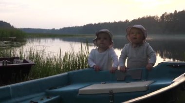 Cute twins in bucket hats happily playing with a boat at the lake . Special moments of life . 