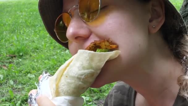 Stylová dívka v kbelíku klobouk a žluté sluneční brýle kousání její zábal s velkou chutí k jídlu venku — Stock video