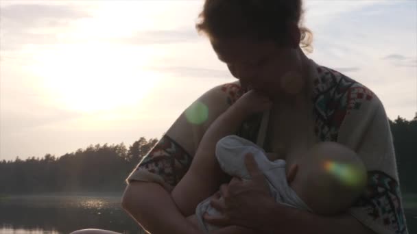 어린 엄마는 선착장에서 호수의 부두에서 아기에게 모유를 먹이고 있다. 아기 와의 유대 시간. — 비디오