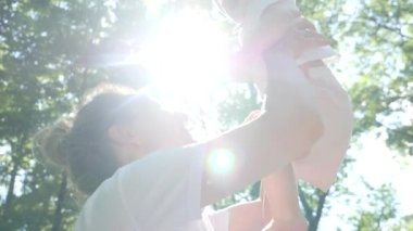 Happy young mom throws her baby girl up on sunny day at the park. Happy family concept. 