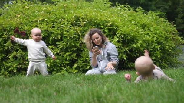 Jovem mãe olhando para seu smartphone ignorando seus gêmeos bebê brincando no parque. Família feliz — Vídeo de Stock