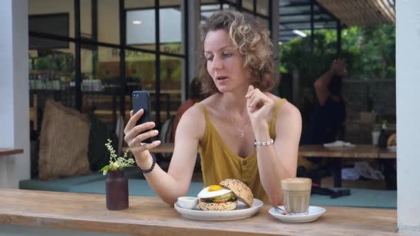 Ung vit kvinna videochattar under sin vegan lunch på utomhus sittning av restaurangen — Stockvideo