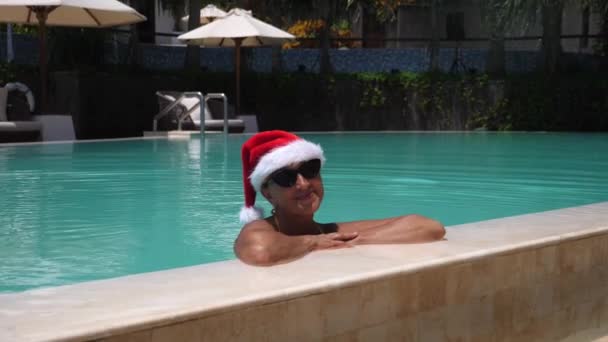 Passer les vacances de Noël sous les tropiques. Heureuse femme d'âge moyen dans le chapeau Santa relaxant une piscine privée — Video