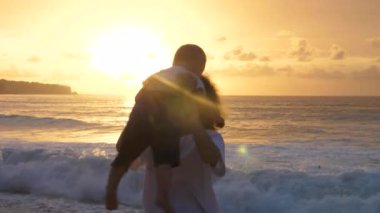 Genç anne bebeğini okyanusun kenarındaki güzel güneşe doğru döndürüyor.