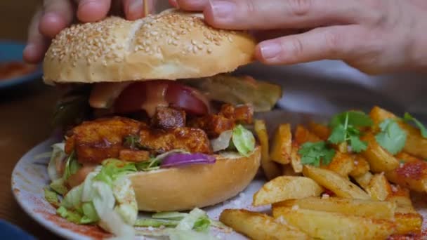 Ręce umieszczając górną bułkę na soczyste wegańskie burger serwowane z frytkami i słodkich frytek ziemniaczanych. Wegańska koncepcja ulicznej żywności — Wideo stockowe