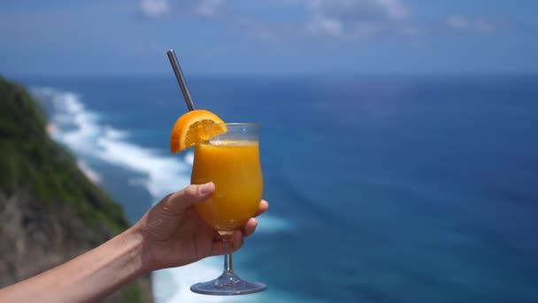 Ręczne trzymanie świeżo wyciśniętego soku pomarańczowego z linią oceaniczną na tle. — Wideo stockowe