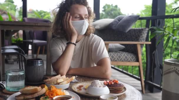 Droevige en eenzame blonde vrouw met een gezichtsmasker aan de volledig bediende tafel die wegkijkt. Depressie veroorzaakt door covid-19 — Stockvideo