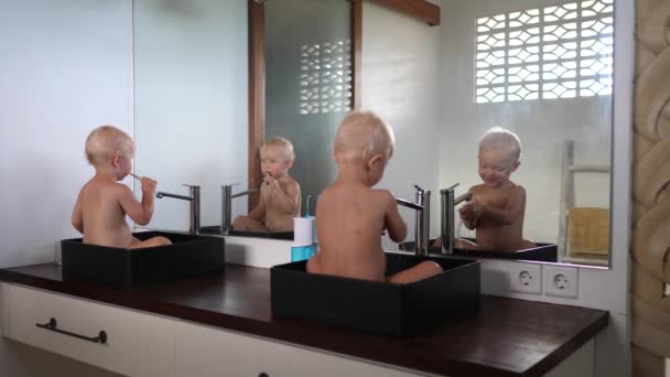 Hygiëne leren van kinds af aan. Twee baby 's in aparte gootstenen poetsen hun tanden en spelen met water — Stockvideo
