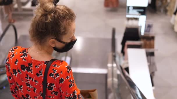 Achteraanzicht van een jonge vrouw met gezichtsmasker die naar beneden gaat op een roltrap in het winkelcentrum. Veilig winkelen tijdens COVID-19 pandemie. — Stockvideo