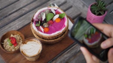 Smoothie hindistan cevizi kasesinin vejetaryen kahvaltısının en üst görüntüsü ahşap tahtada servis ediliyor ve sütsüz latte akıllı telefon ile fotoğraflanıyor. 