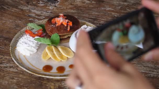 木製のテーブルで提供されるパンケーキや果物の健康的なビーガンの朝食の写真を撮る手 — ストック動画