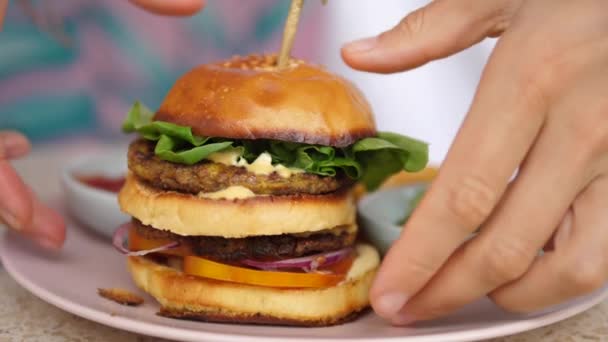 Tangan mengambil tanaman berbasis double-decker burger dari piring. Saus tomat dan kentang goreng disajikan di samping — Stok Video